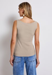 Top senza maniche beige con scollatura rotonda, realizzato in tessuto morbido. Abbinato a jeans a gamba larga di un leggero blu, che mostrano un design casual.