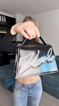 Borsa in pelle verniciata nera con una forma strutturata. Decorata con borchie argentate che formano il nome "Karl" sulla parte anteriore.