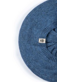 Blue knit beanie with a rounded shape, made of soft yarn. Features a textured finish and a small woven label on the underside.