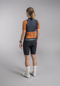 Maillot de cyclisme avec des manches courtes orange et un dos bleu marine, associé à un short noir. Il présente un design ajusté et des chaussettes de sport blanches.