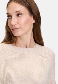Vaaleanpunainen neulepaita, jossa on ribbikuviointi, pyöreä pääntie ja raglan-hihat. Kangas näyttää pehmeältä ja mukavalta hienovaraisilla yksityiskohdilla.