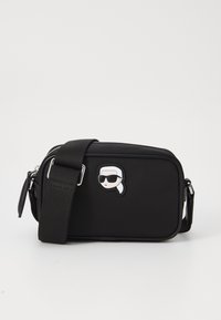 Black fabric crossbody bag with a zip closure, rectangular shape, adjustable strap, and a cartoon patch featuring a head with sunglasses.