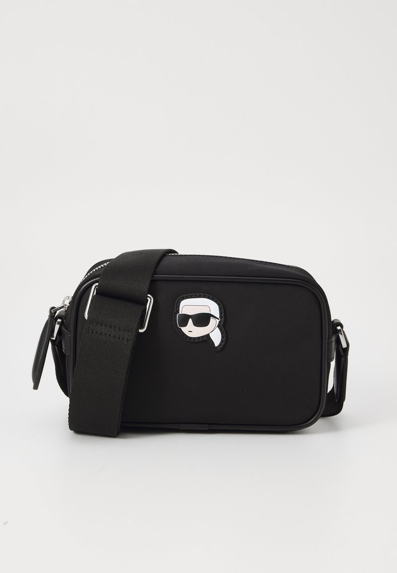Black fabric crossbody bag with a zip closure, rectangular shape, adjustable strap, and a cartoon patch featuring a head with sunglasses.