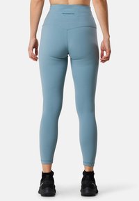 Leggings bleu clair taille haute avec une texture lisse, ornés d'un logo sur la ceinture et d'une coupe ajustée. Associés à des chaussures de sport noires.