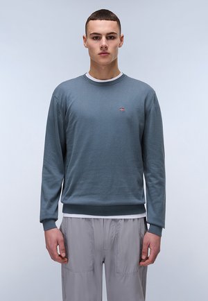 Grijze katoenen trui met een ronde hals, geribbelde manchetten en onderrand, met een klein logo-opdruk. Gelaagd over een wit shirt met zichtbare naden.