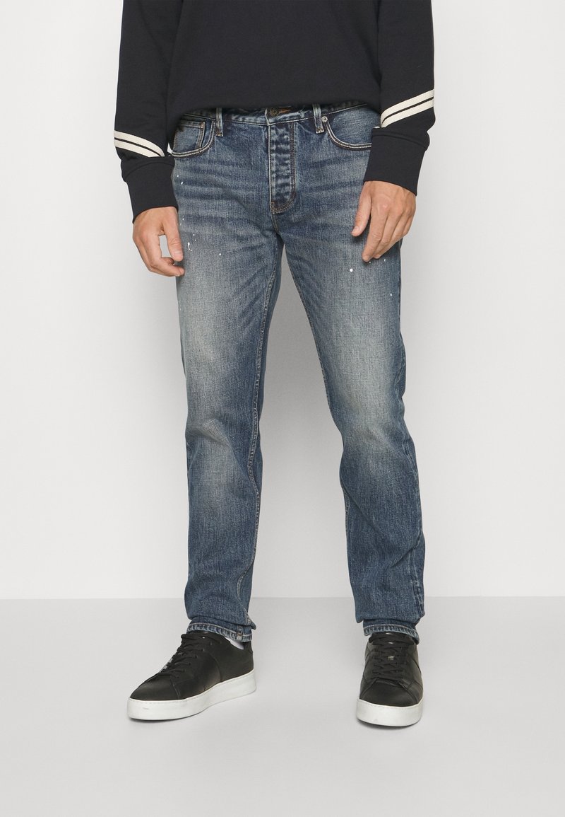 Blå denimjeans med en avslappnad passform, med subtil blekning och lätta färgstänk. Matchas med svarta sneakers och en långärmad topp i marinblå.