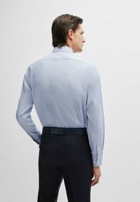 Camicia a maniche lunghe a righe blu e bianche con colletto button-down e texture liscia, abbinata a pantaloni eleganti scuri e una cintura.