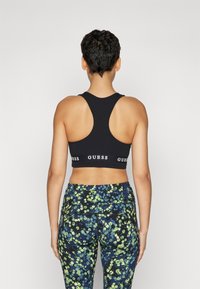 Top deportivo negro de corte corto con diseño de espalda nadadora, que cuenta con una banda elástica con marca. Combinado con leggings de cintura alta en un colorido patrón floral.
