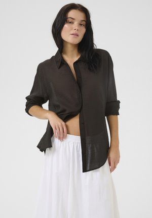 Zwarte, lichte button-up shirt met een ontspannen pasvorm, opgerolde mouwen en een iets doorschijnende textuur, gecombineerd met een witte, luchtige rok.