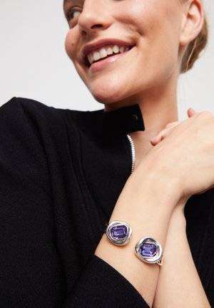 Brazalete de plata con dos piedras rectangulares moradas, con una superficie lisa y pulida y acentos metálicos de forma orgánica.