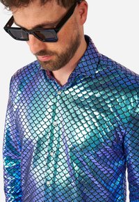 La camicia presenta un motivo a squame iridescenti blu e verdi, realizzata in un tessuto lucido con chiusura a bottoni e colletto appuntito.