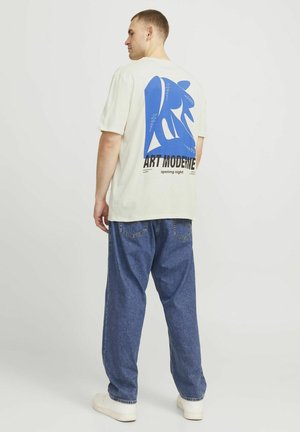 Cream t-shirt with blue graphic print and text "ART MODERNE opening night" on the back, paired with loose-fitting blue denim pants.