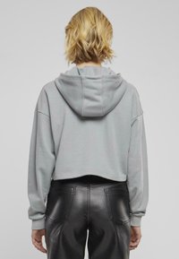 Felpa grigia corta con cappuccio regolabile, maniche larghe e polsini a costine. Indossata con pantaloni neri in finta pelle dotati di tasche posteriori.