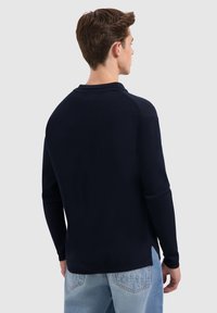 Marineblauwe lange mouwen shirt met een ronde halslijn, voorzien van een gladde textuur en raglanmouwen, gecombineerd met lichtblauwe jeans.