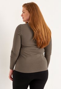 Langsleeve, aansluitend shirt in olijfgroen, gemaakt van zacht materiaal met een ronde halslijn en subtiele plooien op de schouders.
