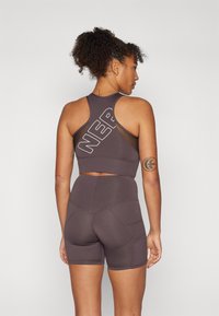 Top desportivo cropped castanho escuro com detalhes em rede e grande gráfico 'NER', combinado com calções de cintura alta em sintonia com detalhes de costura.