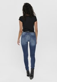 Kapeittavat siniset farkut haalistuneella kuviolla, joissa on kaksi takataskua, yhdistetty mustaan t-paitaan ja mustiin nilkkabootseihin.