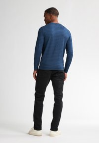 Cămașă albastră cu dungi, cu mânecă lungă și decolteu rotund, asortată cu blugi negri din denim și adidași albi, văzută din spate.