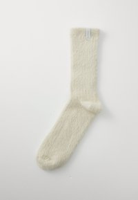 Calzini color crema con una texture soffice, caratterizzati da un design a coste e un piccolo etichetta del marchio sul risvolto.