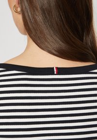 Mustavalkoinen raidallinen paita, jossa on ribbikuvio ja leveä kaula-aukko. Selkäpuolella on pieni punavalkoinen korostustagi.