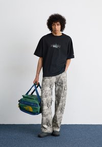 Svart oversized T-skjorte med grafisk logo, lysegrå camoflage cargo-bukser og en grønn duffelbag med gul skrift. Myk tekstur, avslappet passform.