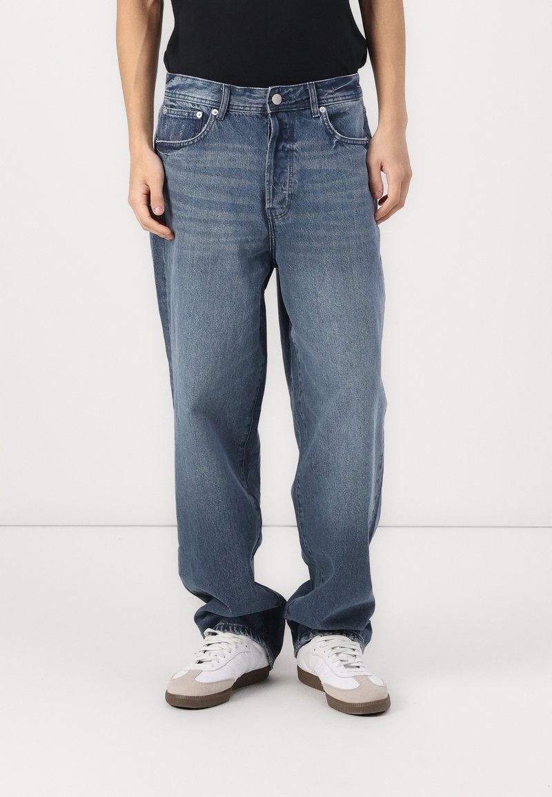 Blå vide bukser laget av denim, med et klassisk femlommersdesign, lys vask og en lett falmet tekstur, supplert med en knappelukking.