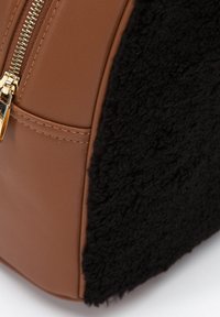 Hnědá kabelka z umělé kůže s černým huňatým bokem, vybavená zlatým zipem a hladkým povrchem. Čtvercový tvar s propracovanými švy.