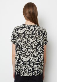 Schwarze Bluse mit kurzen Ärmeln und cremefarbenem Pünktchenmuster, mit Rundhalsausschnitt und subtilen Raffungen an der Rückseite für zusätzliche Textur.