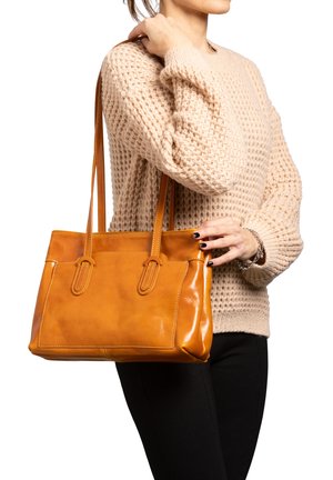 Tan leren schoudertas met twee handvatten, rechthoekige vorm, gladde textuur en contrasterende stiksels; gecombineerd met een gebreid beige truitje.