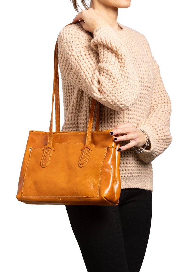 Borsa tote in pelle color tan con due manici, forma rettangolare, superficie liscia e cuciture a contrasto; abbinata a un maglione lavorato a maglia beige.