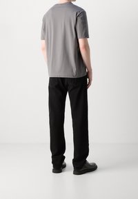 Grå t-shirt med kort ärm och en slät yta, tillsammans med svarta byxor. Outfiten avslutas med svarta skor, sedd fr ån baksidan.