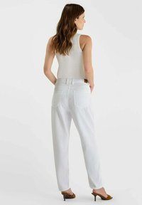 Witte hoge taillebroek met een losse pasvorm, voorzien van achterzakken en een zichtbare tailleband. Gecombineerd met een witte mouwloze top.