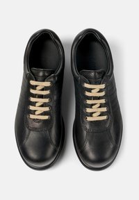 Par de zapatillas de cuero negro con cordones beige, punteras redondeadas y sutiles detalles de costura, mostradas desde arriba sobre un fondo blanco.