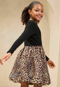 Haut noir à manches longues avec une jupe imprimée léopard, dotée d'une taille froncée et d'une forme évasée, fabriquée en tissu lisse.