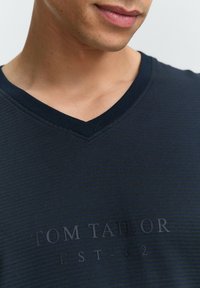 Navy V-Ausschnitt T-Shirt aus geripptem Stoff mit strukturierter Oberfläche. Mit geprägt "TOM TAILOR EST-62" Logo auf der Vorderseite.