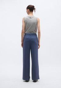 Γκρι αμάνικη μπλούζα σε συνδυασμό με φαρδιά, ψηλόμεση μπλε ναυτικού χρώματος παντελόνια. Τα παντελόνια έχουν πίσω τσέπες και ομαλή υφή, κατάλληλα για επίσημη εμφάνιση.