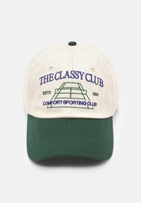 Cappellino da baseball beige con visiera verde. Presenta testo ricamato: "THE CLASSY CLUB" e "COMFORT SPORTING CLUB" insieme a un'illustrazione di un campo da tennis.