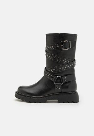 Bottine en cuir noir avec des sangles décoratives, des accents en clous et une boucle rectangulaire. Dotée d'une semelle robuste avec un léger talon.