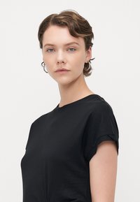 Svart t-shirt med kort ärm och rund halsringning, gjord av mjukt material, med uppvikta ärmar och en enkel design.