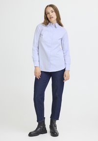 Camicia button-up lilla con maniche lunghe, abbinata a jeans di denim scuro e stivaletti neri alla caviglia con cinghie e fibbie.
