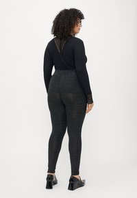 Juodas ilgomis rankovėmis viršus su tinkliniais atgaliais, dėvimi su aukšto liemens, blizgančiais juodais leggingais. Modelis vilki blizgius juodus batelius ant blokinio kulno.