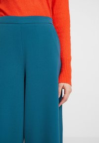 Teal vida byxor med en slät yta och skräddarsydd midja, tillsammans med en orange ribbad tröja, som visar en kontrast i färg.