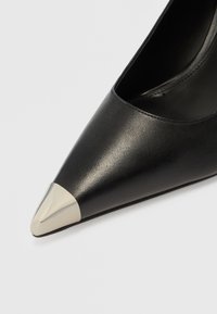 Czarny skórzany but na wysokim obcasie z zakrzywionym noskiem i metaliczną srebrną nakładką na końcu. Gładka tekstura z elegancką sylwetką.