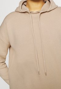 Helle beige Kapuzenjacke aus weichem Strickstoff, mit einer Kapuze und Zugb�ändern mit goldenen Metallenden. Lässiger, entspannter Schnitt.