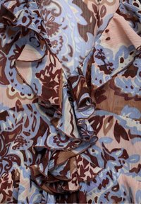 Tissu à motif floral avec des nuances de bleu, marron et rose, bordé de volants et à finition texturée.