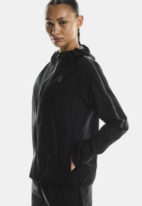 Must melanži kerge jope kapuutsiga, millel on peegeldavad triibud varrukatel ja tõmblukuga ees. Sile, mati tekstuur suurendab funktsionaalsust.