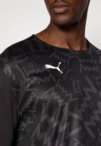 Black athletic shirt featuring textured geometric patterns, a crew neck, and a white Puma logo on the chest. Smooth, lightweight material.