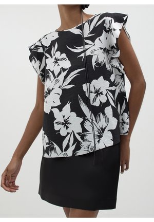 Haut sans manches à motif floral noir et blanc avec épaules volantées, associé à une jupe noire unie sur une personne debout.