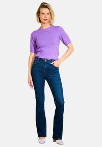 Svetre z raztegljivih niti z kratkimi rokavi v lavandovi barvi, v kombinaciji z oprijetimi temno modrimi jeansom. Jeans imajo ravno obliko nog. Manekenka stoji s roko na boku.