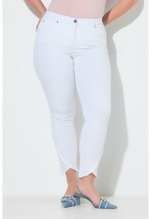 Persona con curvas que lleva vaqueros blancos hasta el tobillo con bajos recortados y zapatos slingback azules de tacón bajo, punta picuda y con adornos.